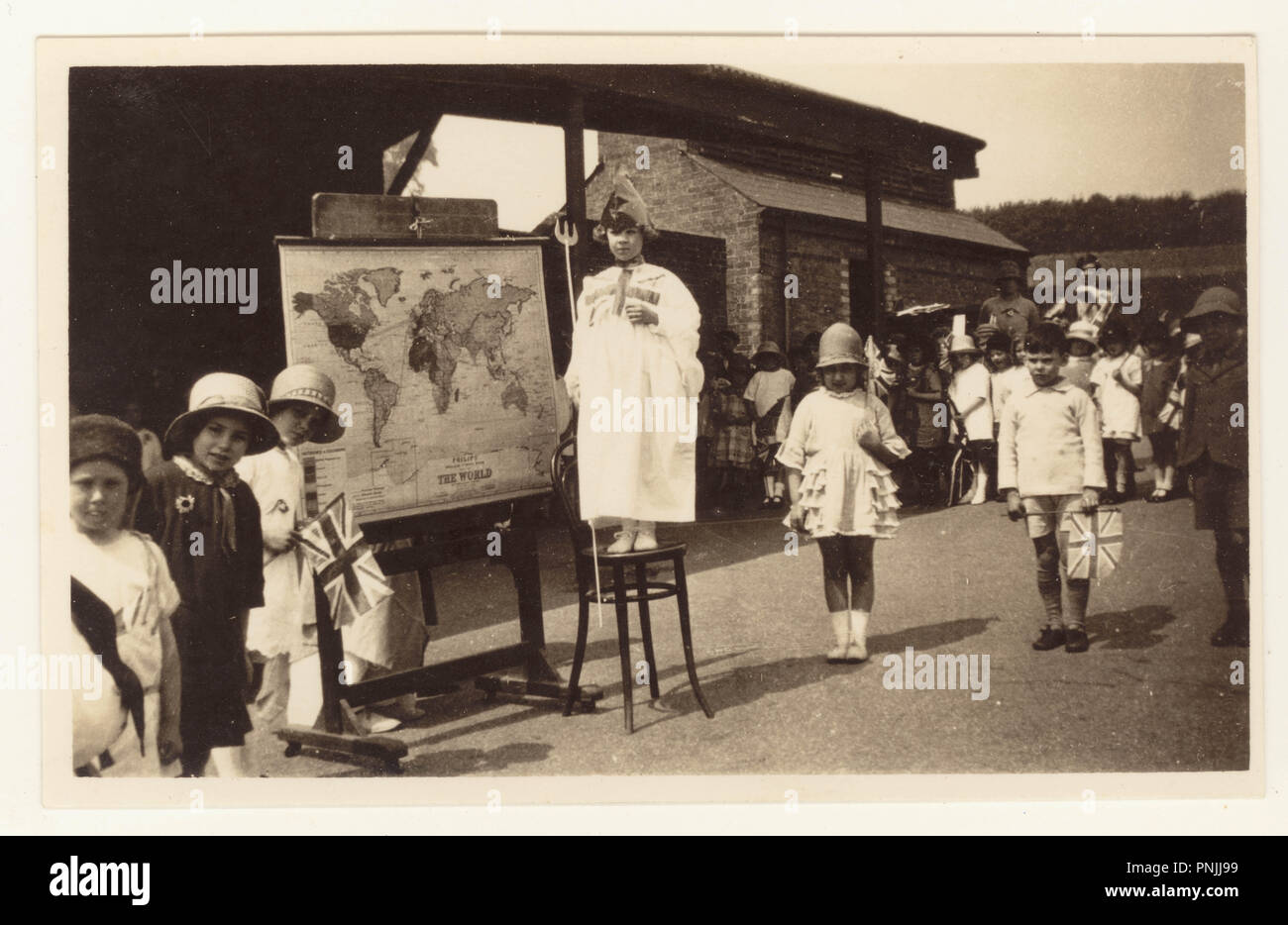 Postkarte von strood Schule Kinder Frieden Fete, Strood, Rochester, Kent, Großbritannien ein Kind im Brittania Kostüm gekleidet und sie steht neben einem Philips Karte der Welt. Die Postkarte, datiert vom 4. August 1919, Stockfoto