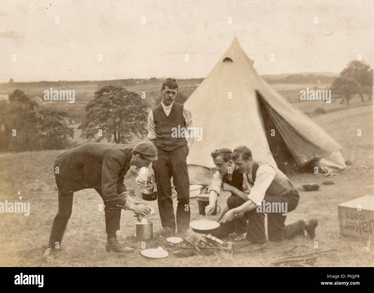 Edwardianische Postkarte von jungen Männern, die auf dem Land campen, Kochen auf offenem Feuer außerhalb Zeltdach, um 1905, Großbritannien Stockfoto