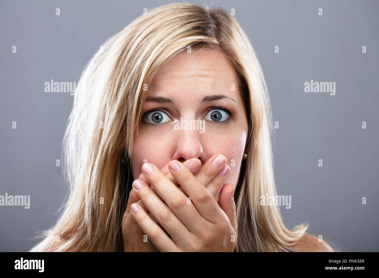 Frau mit der Hand auf den Mund über Grauer Hintergrund Schockiert Stockfoto