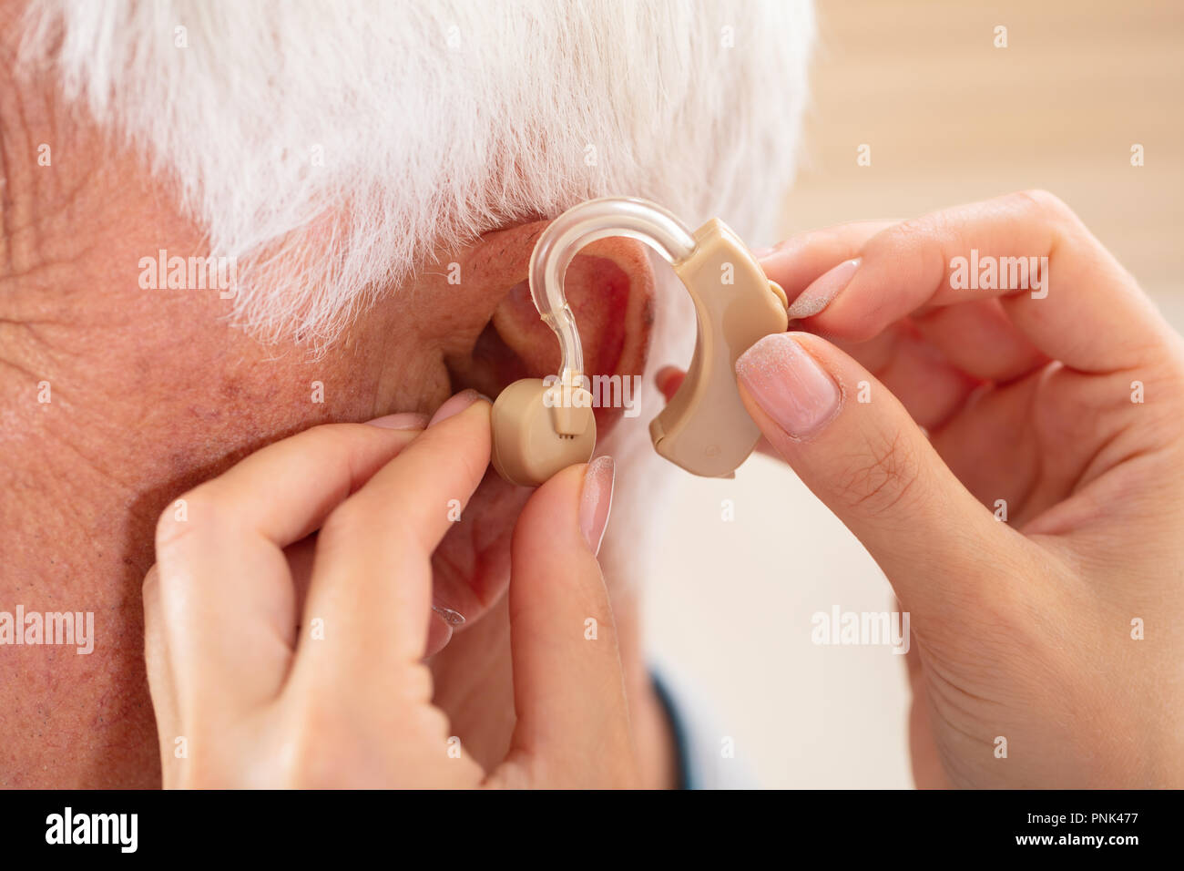 Die Ärztin Hand einfügen Hörgerät im Ohr von männlichen Patienten Stockfoto