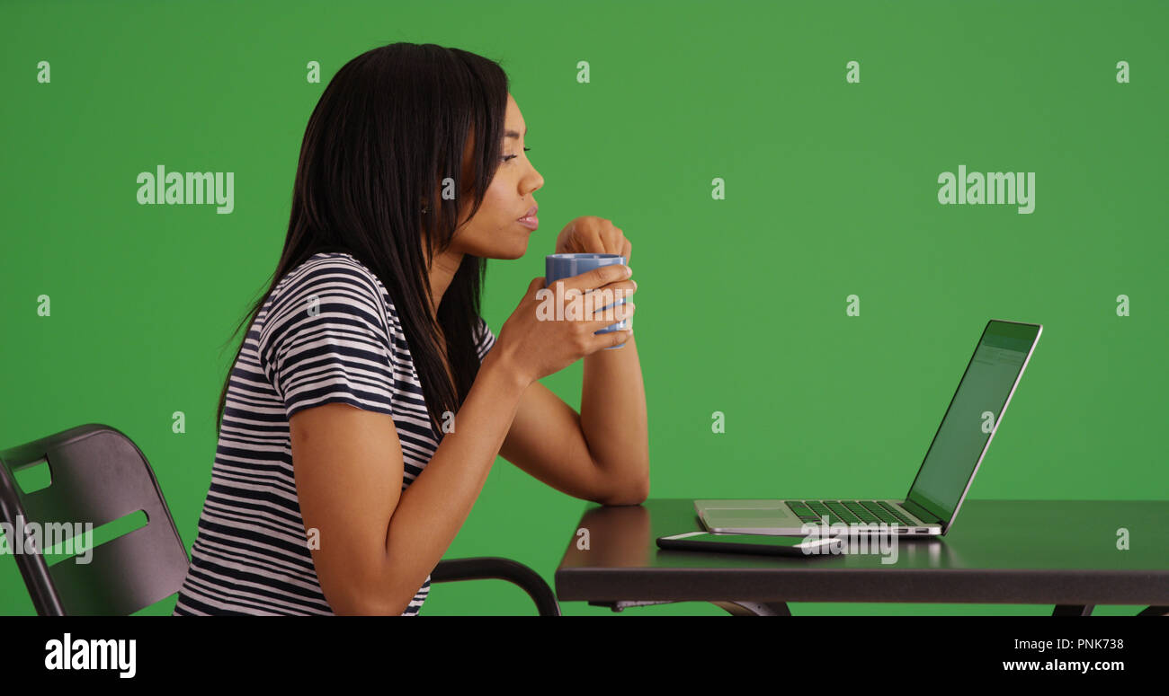 Profil von schwarzes Weibchen sitzen, Kaffee trinken und mit Laptop auf dem Green Screen Stockfoto