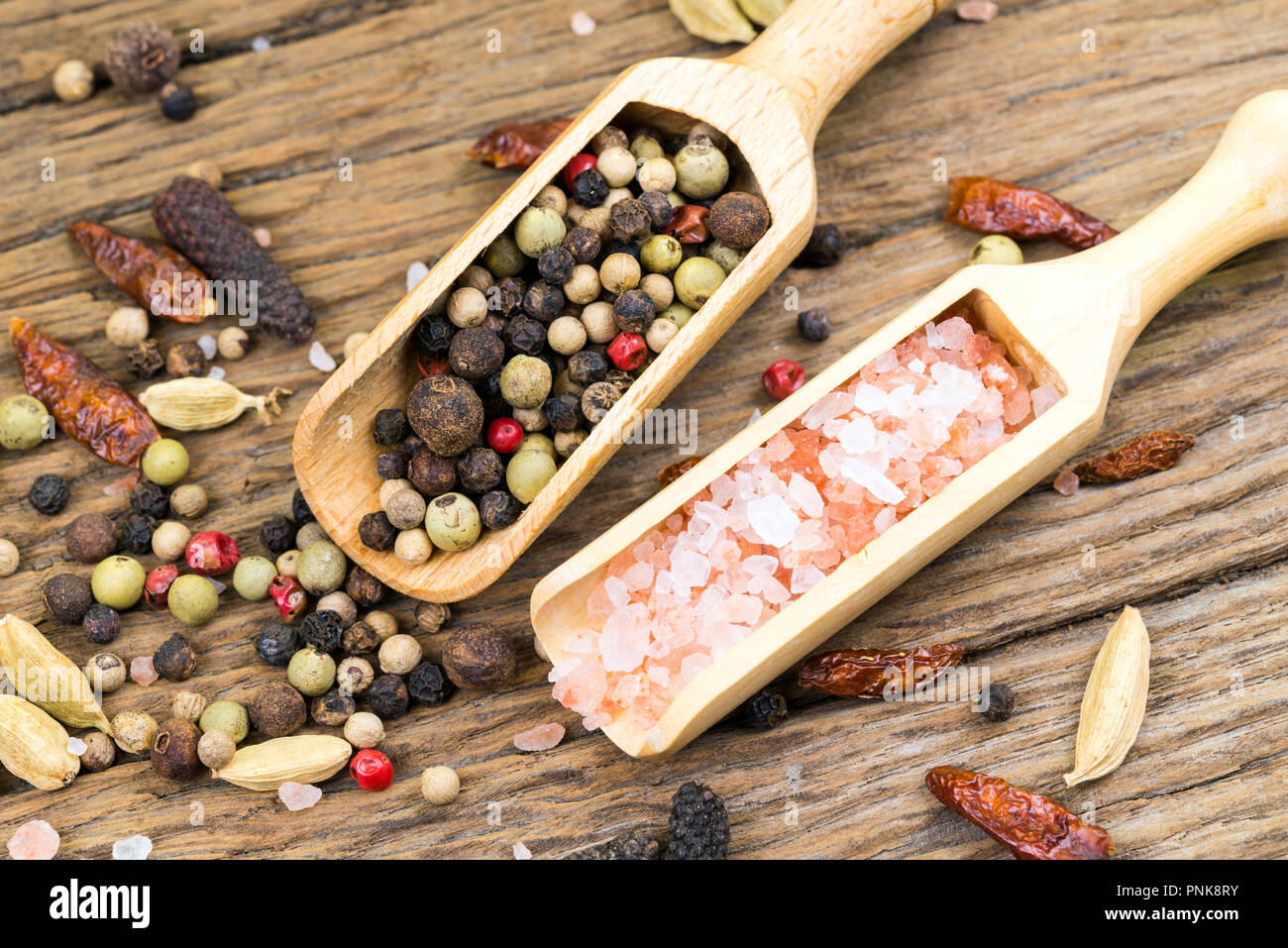 Nahaufnahme der bunte Pfefferkörner und rosa Kristall Salz auf kleinen hölzernen Spice Lufthutzen auf rustikalen Holz Hintergrund mit weiteren Gewürzen Stockfoto