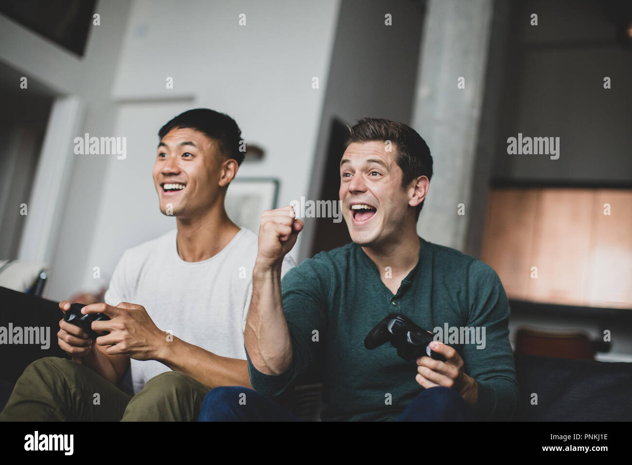 Männliche Freunde spielen auf einer Spielekonsole Stockfoto