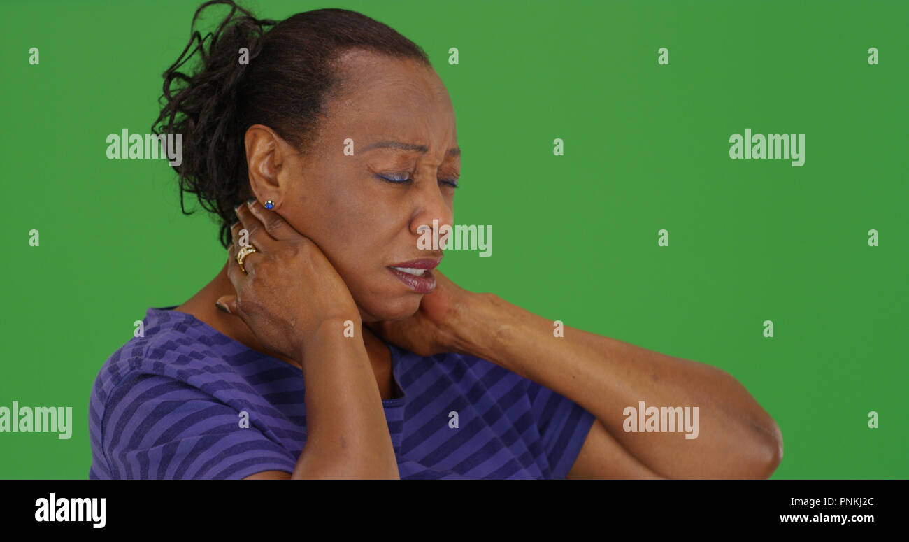 Reife schwarze Frau mit schlechten Nackenschmerzen auf Green Screen Stockfoto
