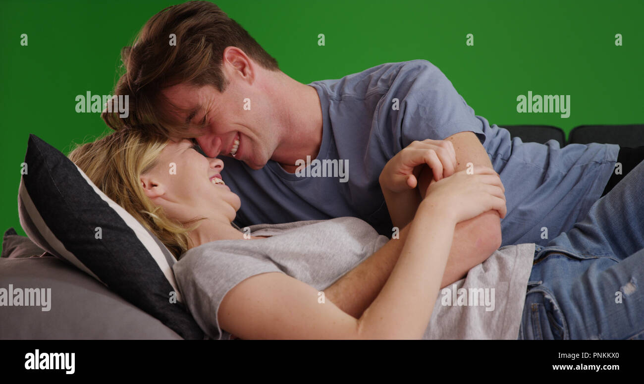 Glückliches junges Paar kuscheln auf der Couch oder Bett Lachen und Lächeln auf Green Screen Stockfoto