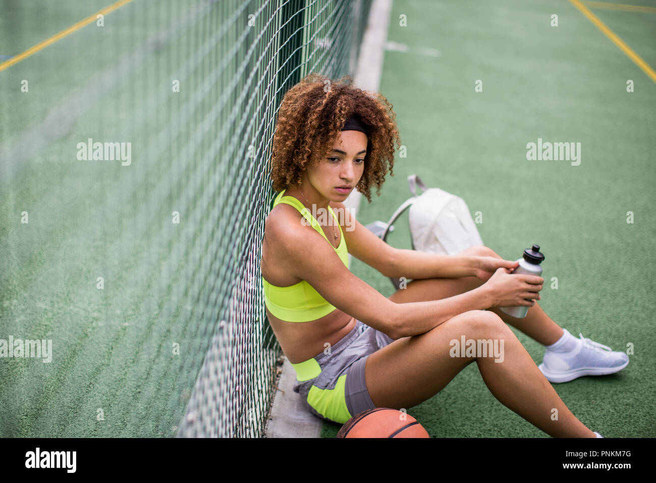 Junge erwachsene Frau sitzt auf einem Basketballplatz Stockfoto