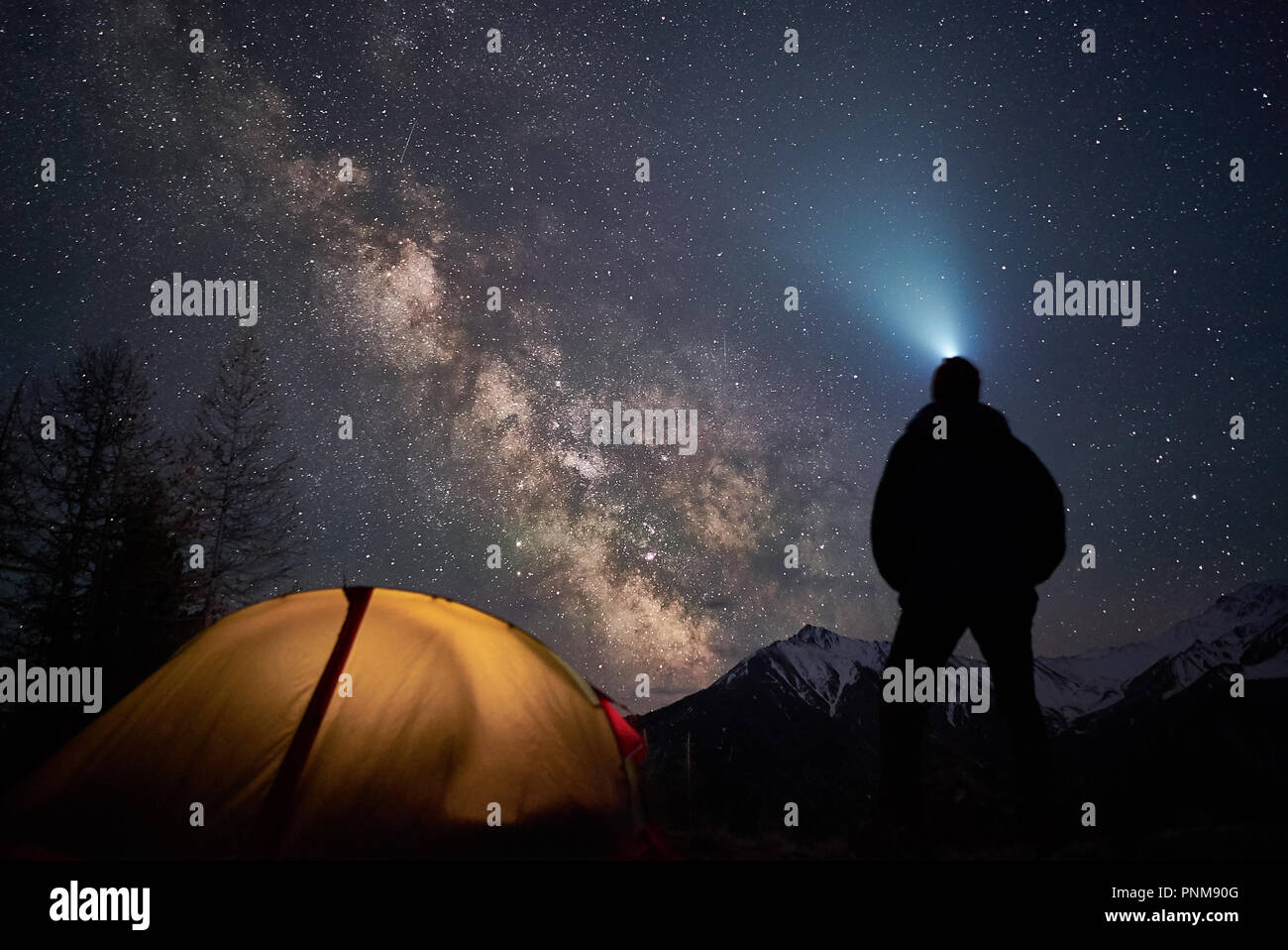 Man Touristen mit Taschenlampe steht in der Nähe von seinem Lager Zelt in der Nacht unter einem Himmel voller Sterne. Stockfoto