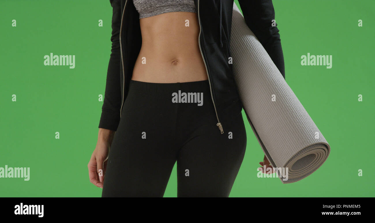 Junge schwarze Frau steht in ihrem Crop Top mit Yoga Matte auf Green Screen Stockfoto