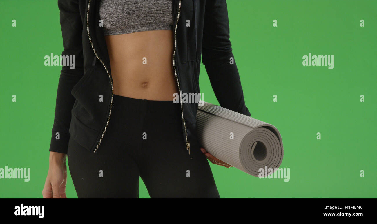 Junge schwarze Frau steht in ihrem Crop Top mit Yoga Matte auf Green Screen Stockfoto