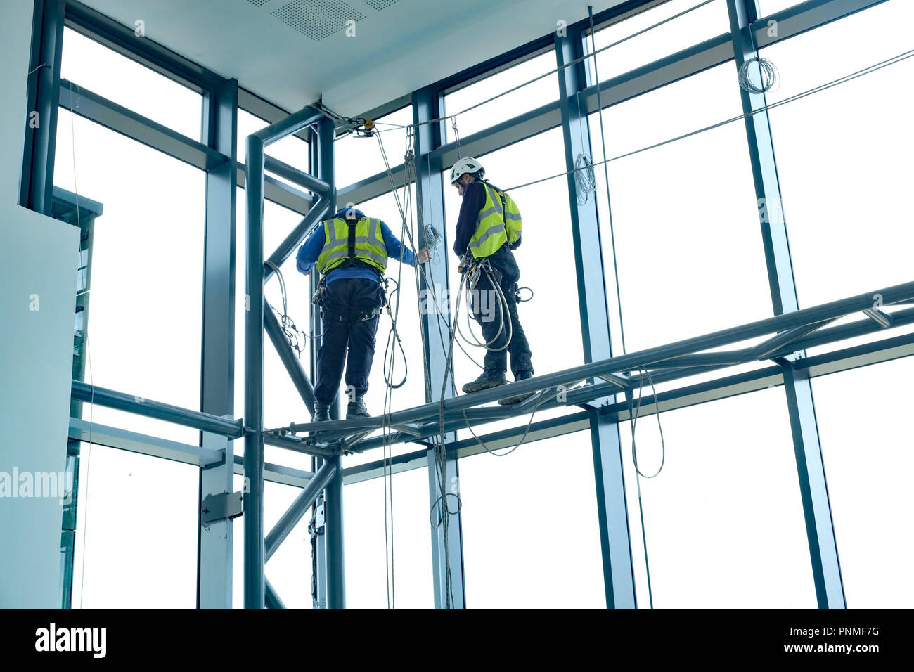 März 2016 - Zwei seilunterstützte Kerle auf hohem Niveau in einem Büro Eingangsbereich arbeiten Stockfoto
