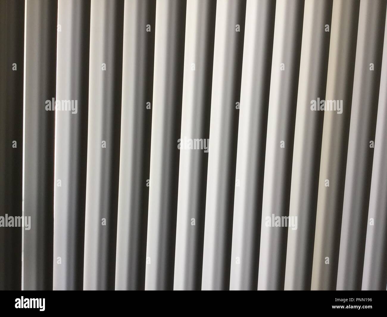 Vertikale Jalousien vor einem schwarzen Hintergrund mit weißen, grauen und schwarzen Leitungen. Stockfoto