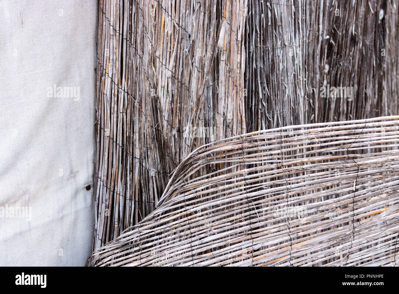 Vintage bamboo rattan Nahaufnahme eines baufälligen Retro getragen Zaun zusammengehalten mit rostigem Draht und weißen Stoff canvas Hintergrund Textur, Muster von Stockfoto