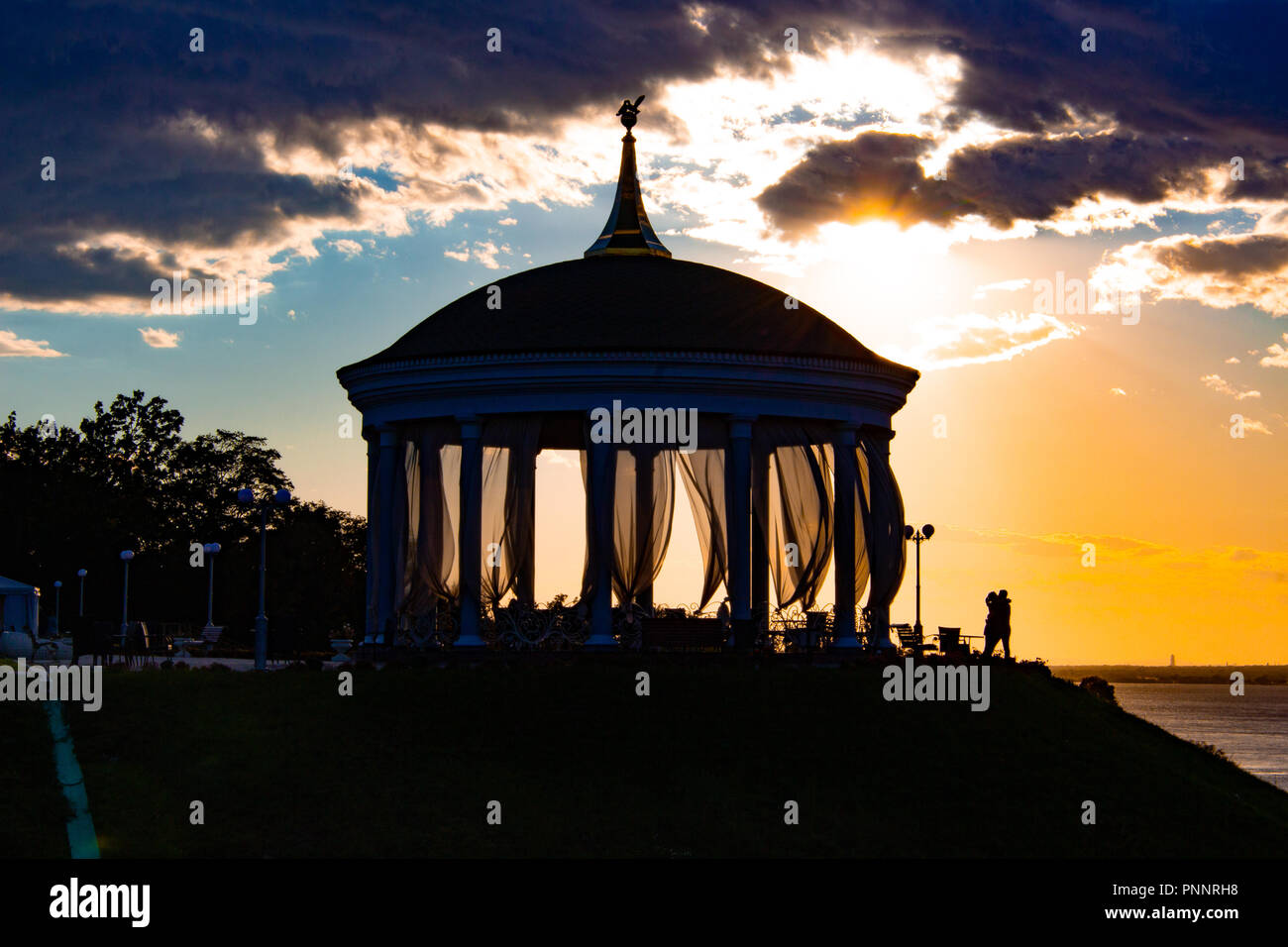 Ein Paar in Liebe Umarmungen und Küsse neben einem romantischen Pavillon gegen den Sonnenuntergang Stockfoto