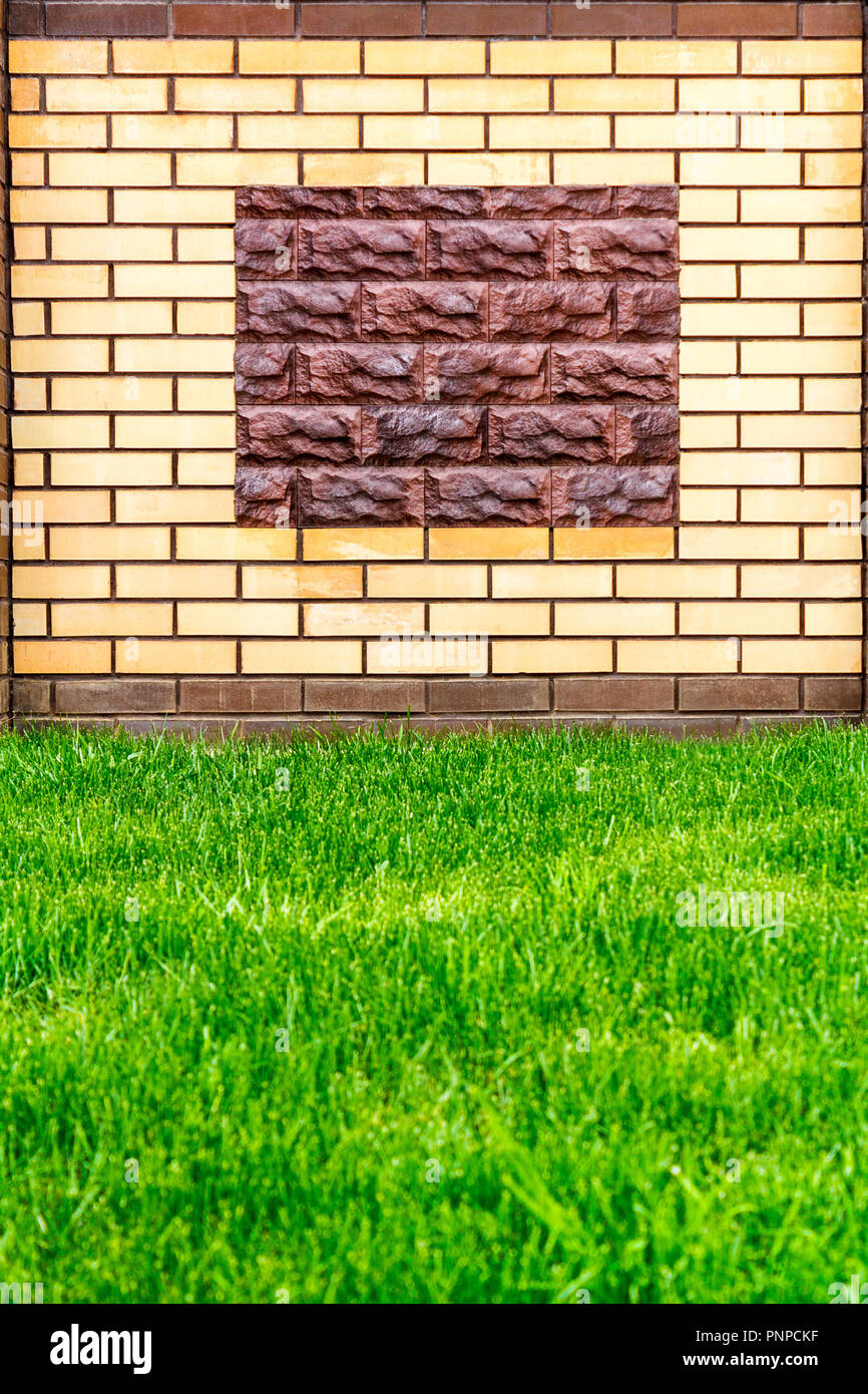 Eine Wand aus Licht aus Backstein mit einem dekorativen braun Stein und grünen Rasen gestaltet. Stockfoto