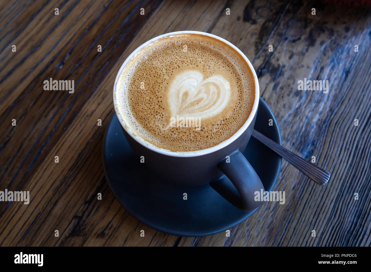 Tasse Kaffee mit Latte Art in Herzform auf hölzernen Tisch Stockfoto