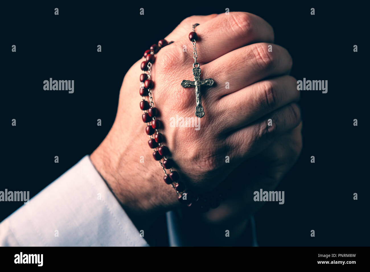 Männliche Hände halten einen Rosenkranz beten mit Jesus Christus am Kreuz oder Kruzifix auf schwarzem Hintergrund. Reifer Mann mit Christian katholischen religiösen Glauben Stockfoto