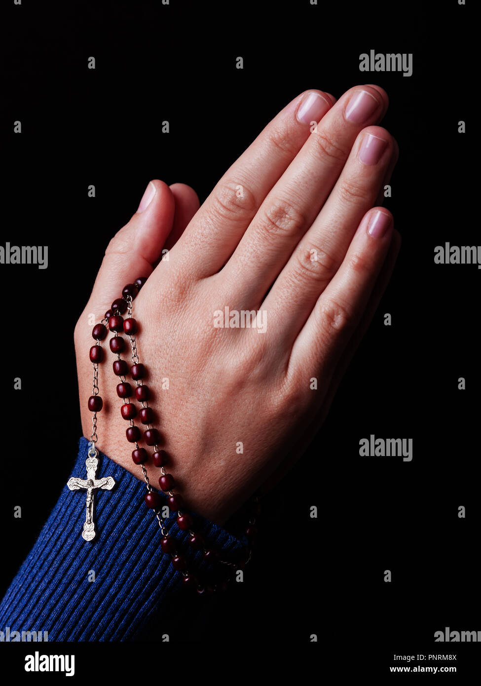 Weibliche Hände halten ein Perlen Rosenkranz beten mit Jesus Christus am Kreuz oder Kruzifix auf schwarzem Hintergrund. Frau mit christlichen und katholischen Religionslehrern fa Stockfoto