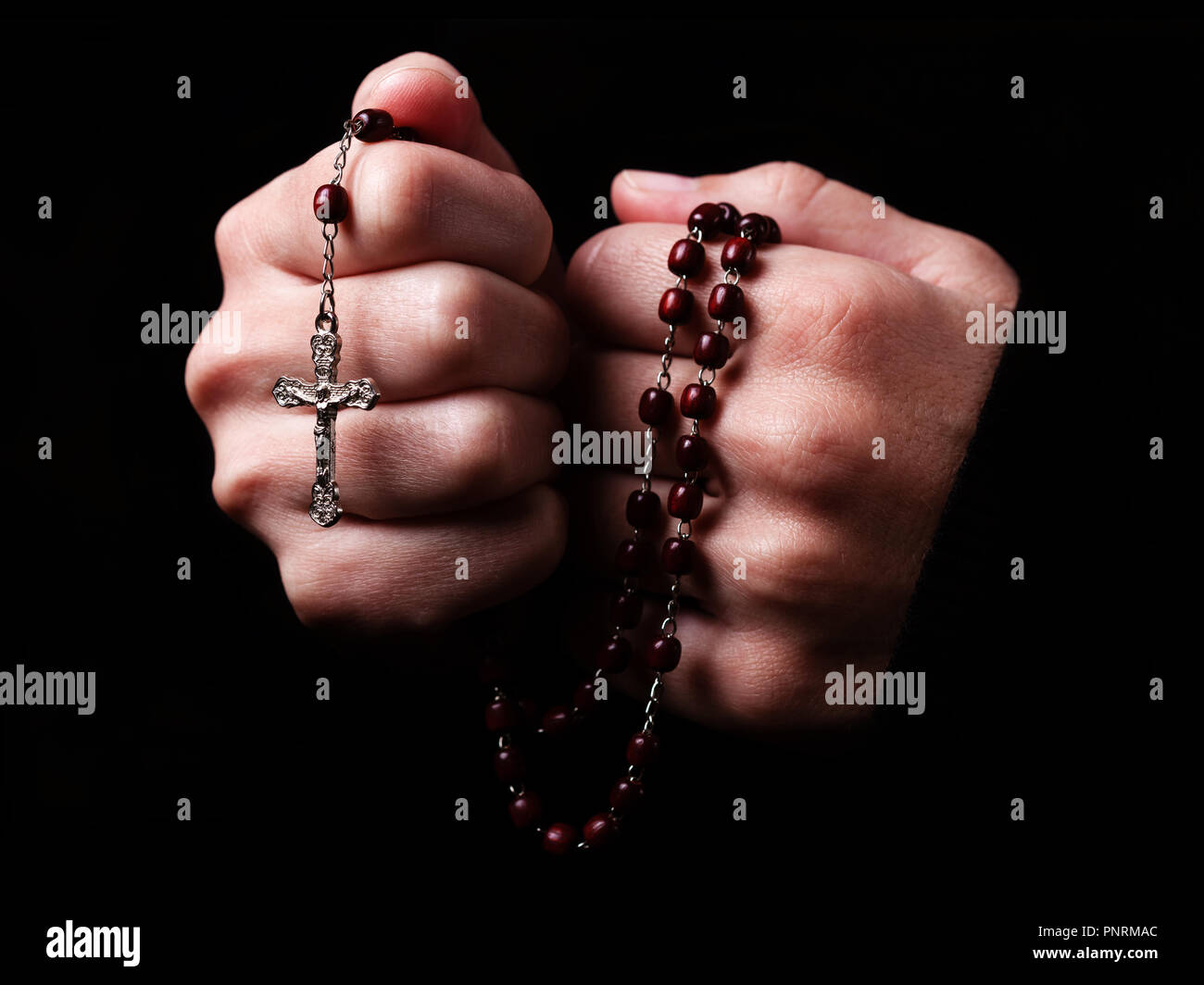 Weibliche Hände halten einen Rosenkranz beten mit Jesus Christus am Kreuz oder Kruzifix auf schwarzem Hintergrund. Frau mit Christlichen katholischen religiösen Glauben Stockfoto