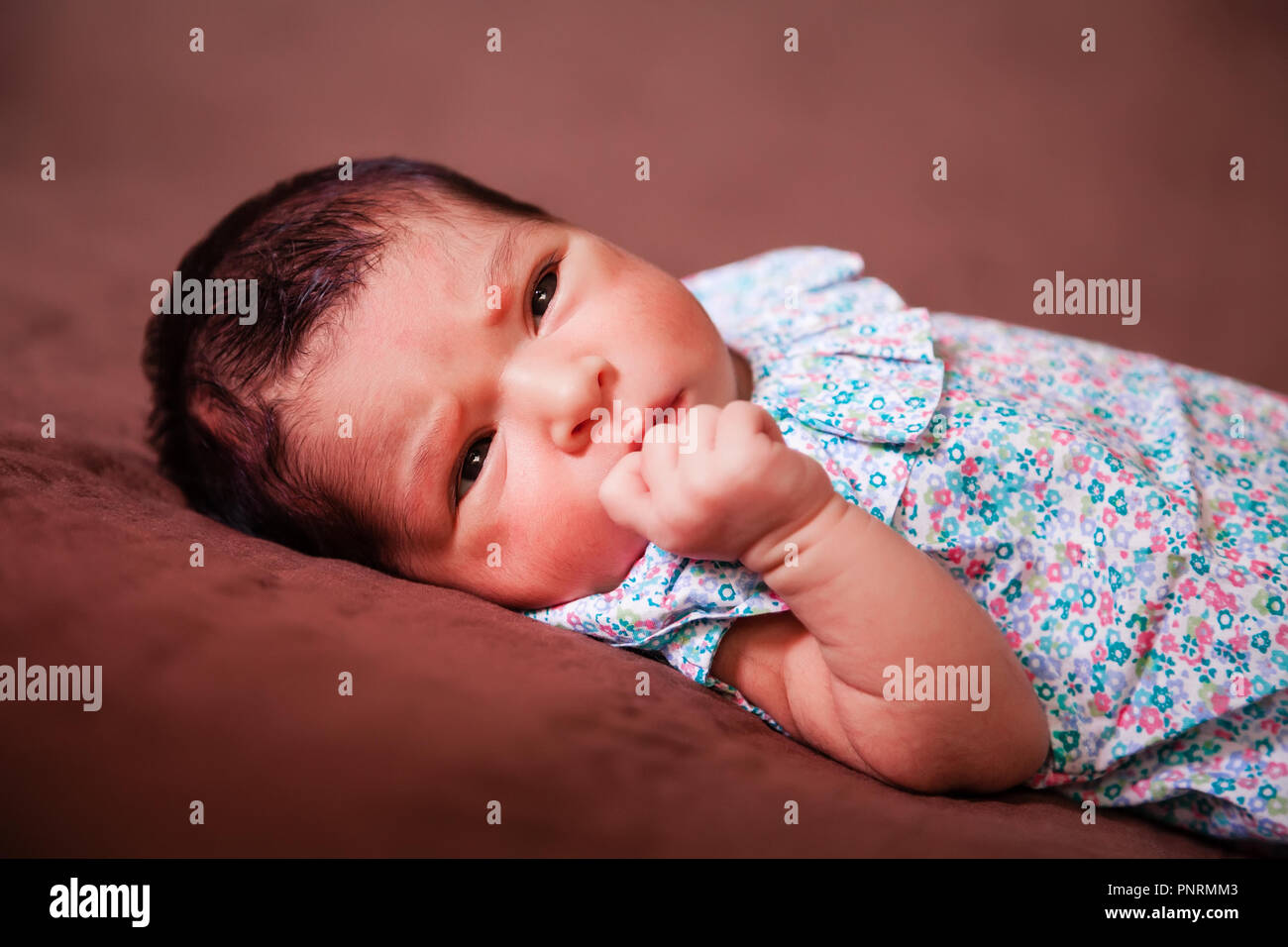 Nahaufnahme, Porträt einer niedlichen Zwei Wochen alte Neugeborene Mädchen hinlegen, die Augen öffnen und Suchen rund um das Tragen eines geblümten Kleid Stockfoto