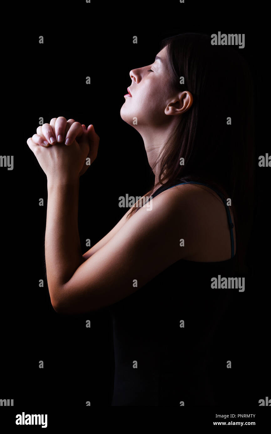 Treue Frau zu beten, die Hände gefaltet in der Anbetung mit Kopf auf und geschlossenen Augen in religiösem Eifer für Gott, auf einem schwarzen Hintergrund. Konzept für Religion, Stockfoto