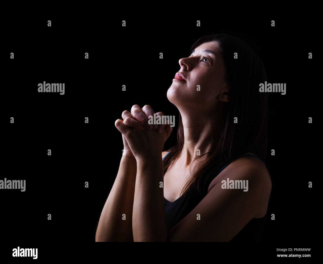 Treue Frau zu beten, die Hände gefaltet in der Anbetung mit bis Suchen in religiösem Eifer für Gott, auf einem schwarzen Hintergrund. Konzept für Religion, Glauben, Gebet Stockfoto
