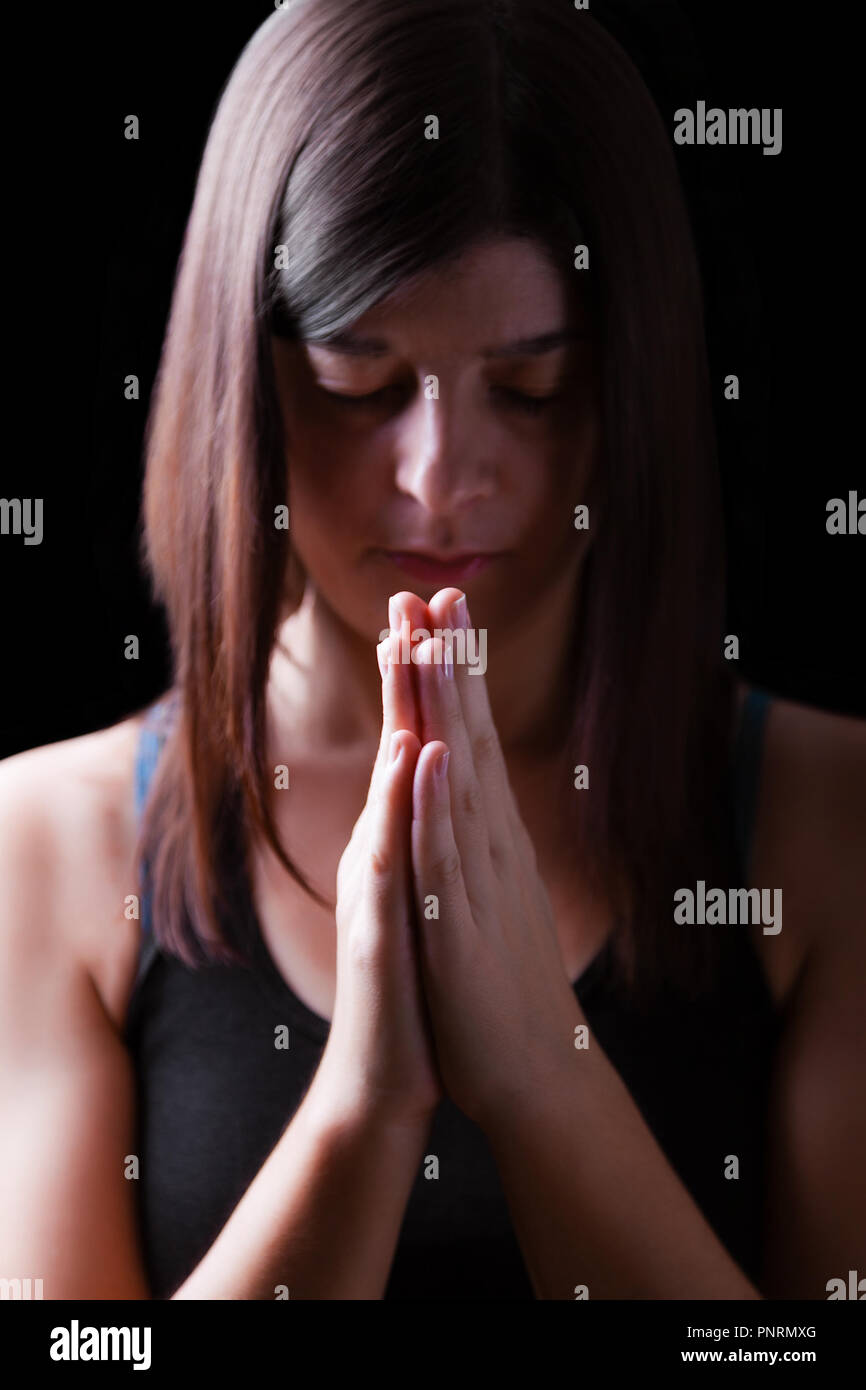 Gläubigen athletische Frau beten, mit Händen in Anbetung zu Gott gefaltet, Kopf und Augen in religiöser Inbrunst geschlossen, auf schwarzen Hintergrund. Konzept für Stockfoto
