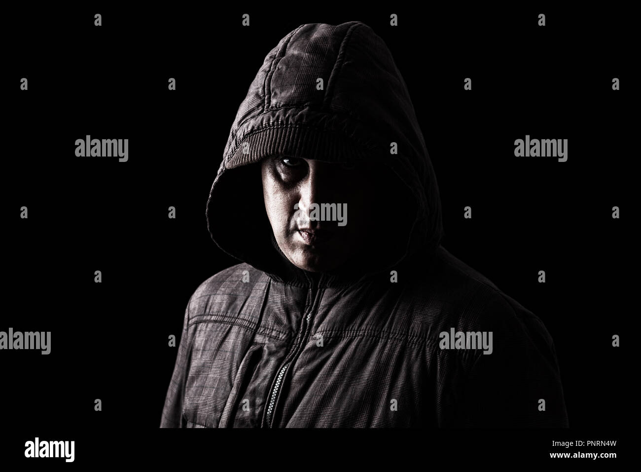 Beängstigend Kaukasischen oder Weiß reifer Mann versteckt sich in den Schatten, mit dem Gesicht zum Teil mit der Haube verborgen, und stehen in der Dunkelheit. Schwarzen Hintergrund. Stockfoto
