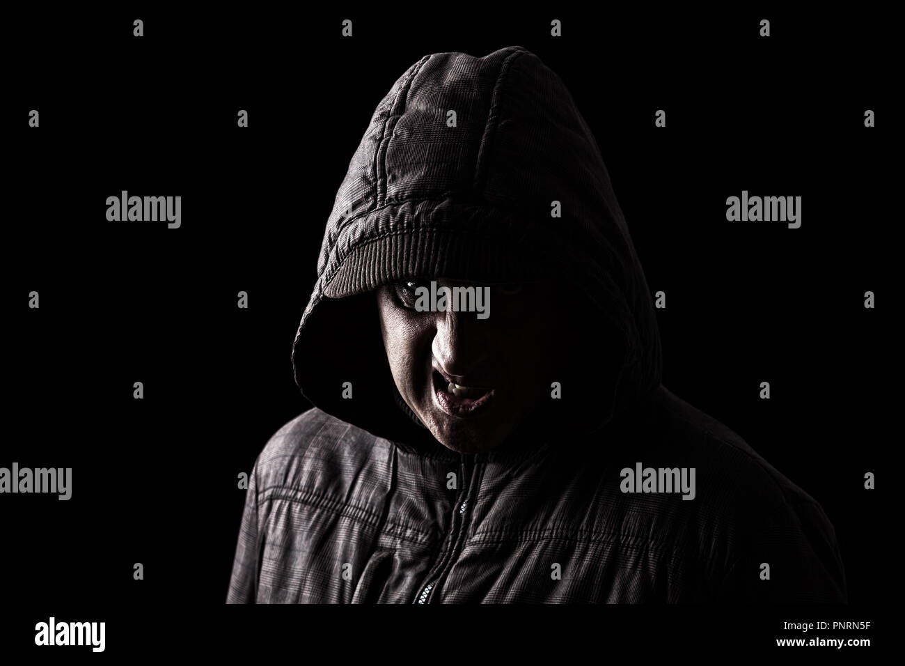 Sehr wütend und aggressiv Mann versteckt sich in den Schatten, mit dem Gesicht zum Teil mit der Haube verborgen, und stehen in der Dunkelheit. Low Key schwarzer Hintergrund Stockfoto