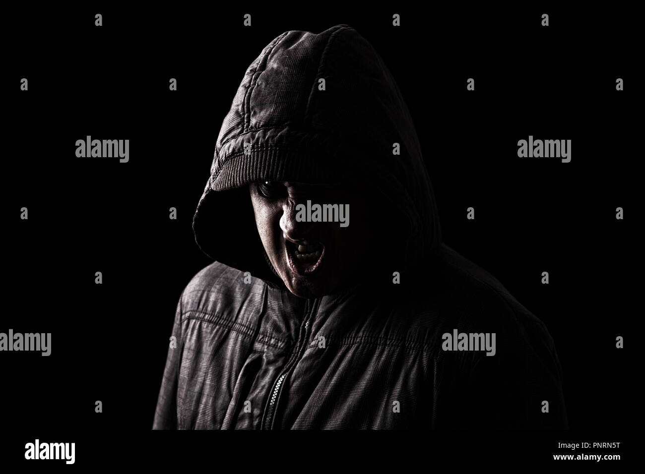 Sehr wütend und aggressiv Mann versteckt sich in den Schatten, mit dem Gesicht zum Teil mit der Haube verborgen, und stehen in der Dunkelheit. Low Key schwarzer Hintergrund Stockfoto
