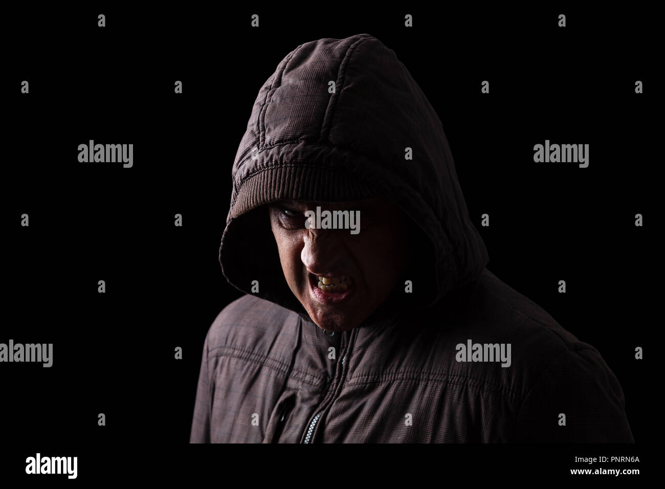 Sehr wütend und aggressiv Mann versteckt sich in den Schatten, mit dem Gesicht zum Teil mit der Haube verborgen, und stehen in der Dunkelheit. Low Key schwarzer Hintergrund Stockfoto