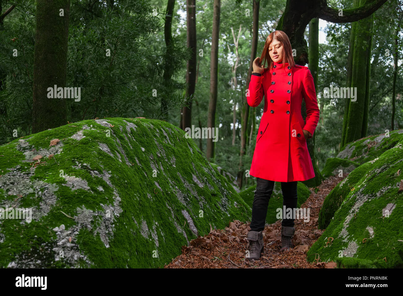 Junge Frau traurig alleine auf den Waldweg das Tragen der roten langen Mantel oder Jacke. Mädchen geht auf Spaziergang in den Wäldern des Naturparks im Herbst, Stockfoto
