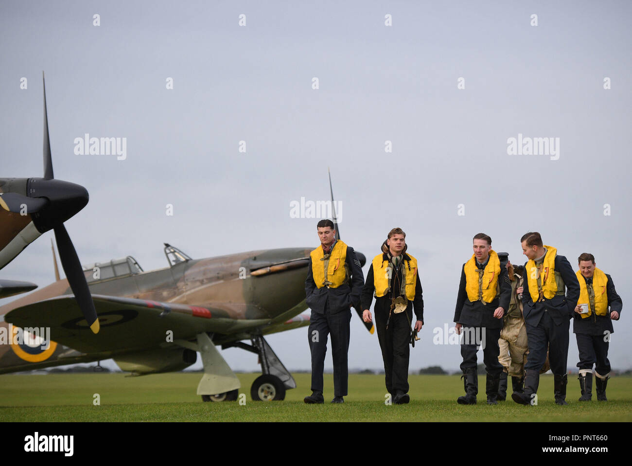 Historische reenactment Mitglieder aus Geist von Großbritannien zu Fuß vorbei an einer Hawker Hurricane auf der Flucht vor der Schlacht von Großbritannien Air Show im Imperial War Museum in Duxford, Cambridgeshire. Stockfoto