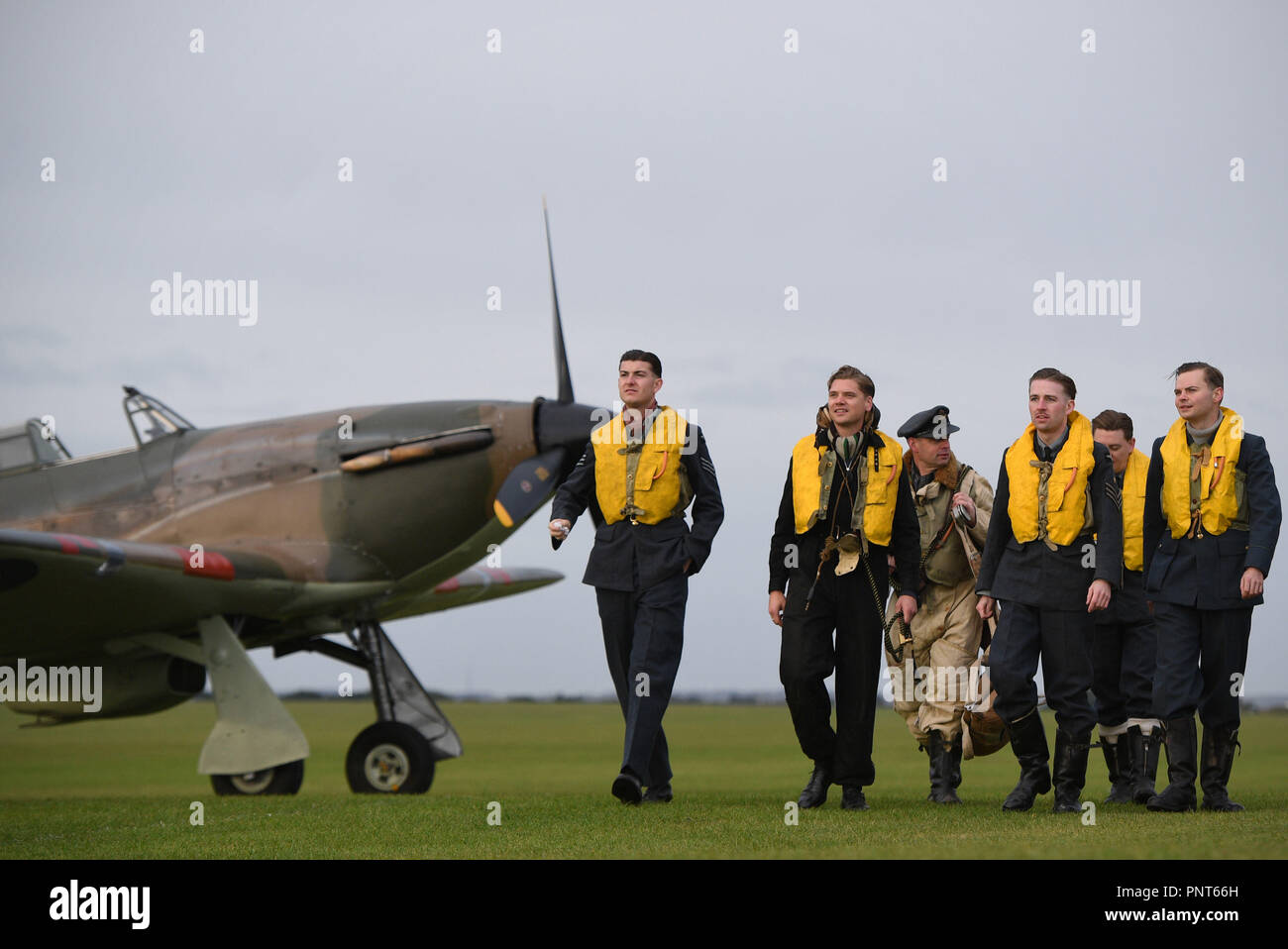 Historische reenactment Mitglieder aus Geist von Großbritannien zu Fuß vorbei an einer Hawker Hurricane auf der Flucht vor der Schlacht von Großbritannien Air Show im Imperial War Museum in Duxford, Cambridgeshire. Stockfoto