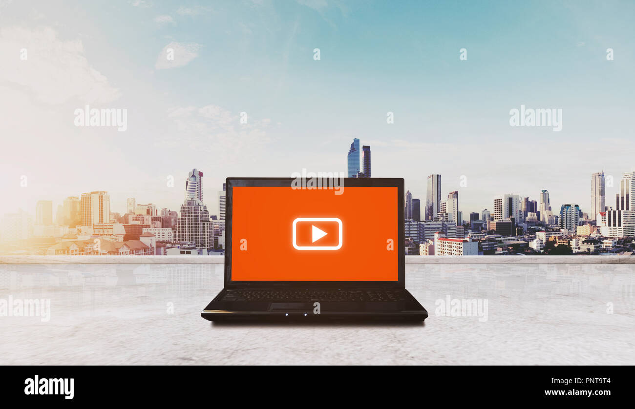 Online Medien- und Anwendungstechnik. Computer Laptop auf der Dachterrasse mit Media play Symbol auf dem Bildschirm und Stadt sunrise anzeigen Stockfoto