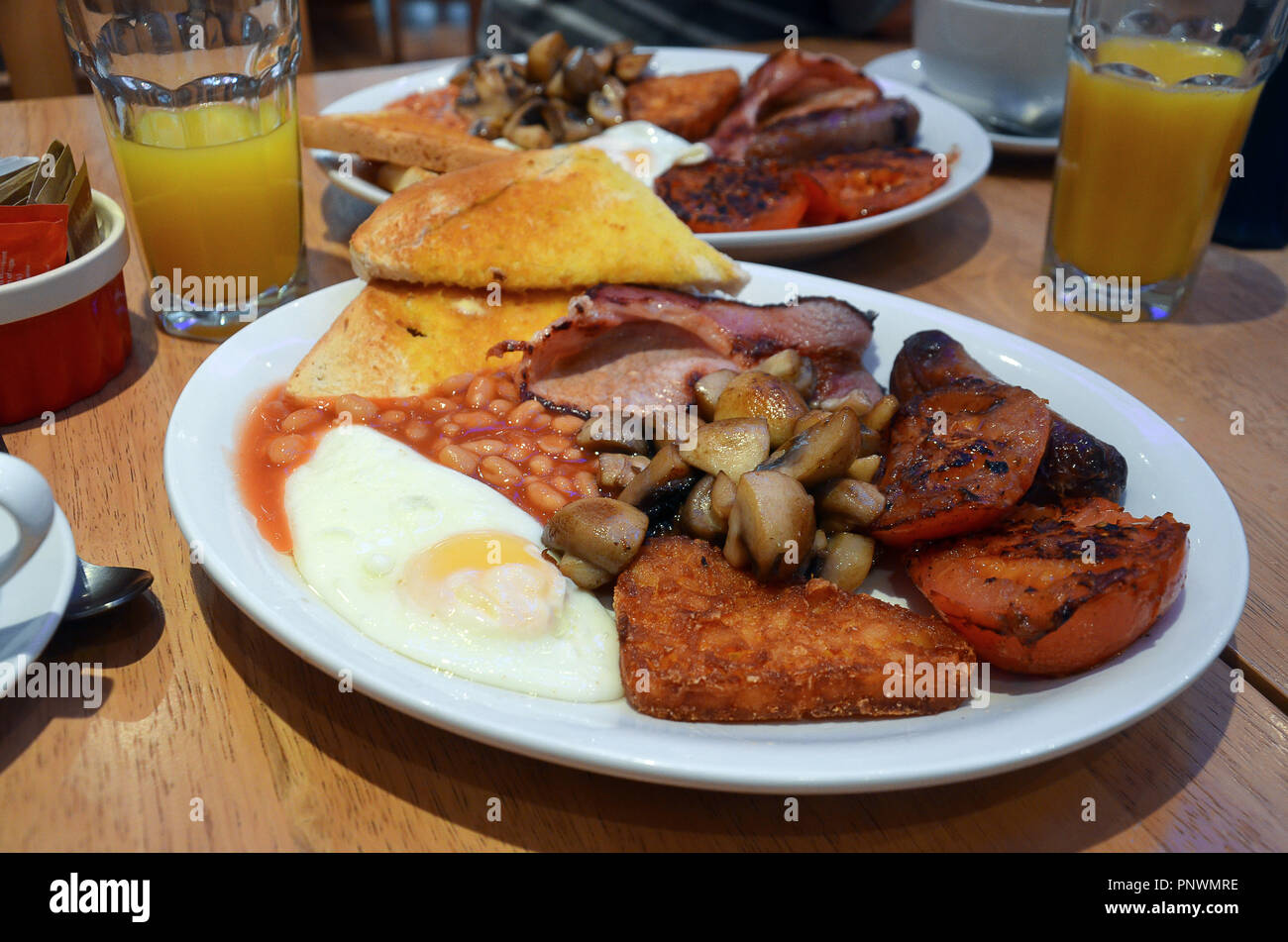 Komplettes englisches Frühstück für Zwei, mit gebratenen Eiern, Toast, Pilze, Tomaten, Würstchen, Bohnen, Hash Browns und Orangensaft Stockfoto