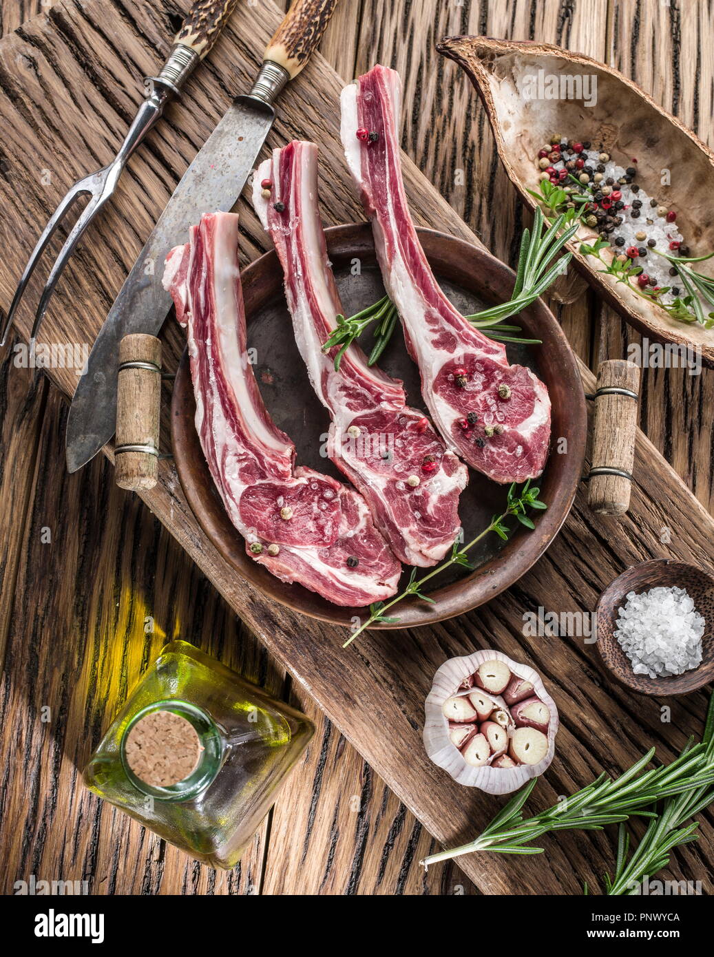 Rohe Lammkoteletts mit Knoblauch und Kräutern auf dem alten Holztisch. Stockfoto