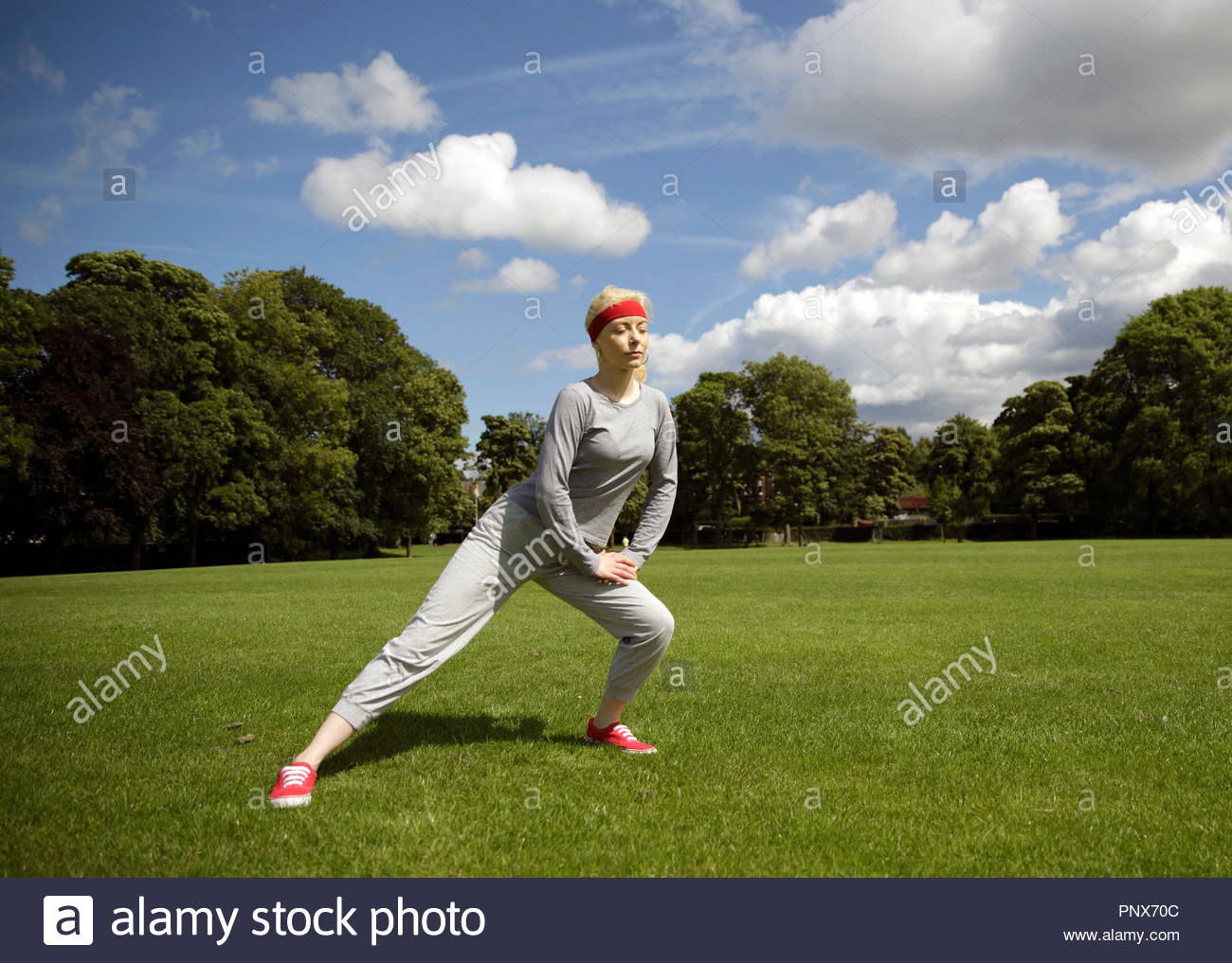Blonde Frau in einem Trainingsanzug ausführen Stretching Übungen im Park Stockfoto