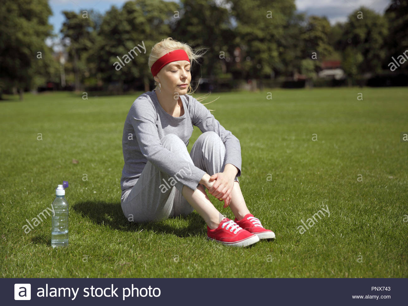 Blonde Frau in einem Trainingsanzug excercising und Sitzen im Park Stockfoto