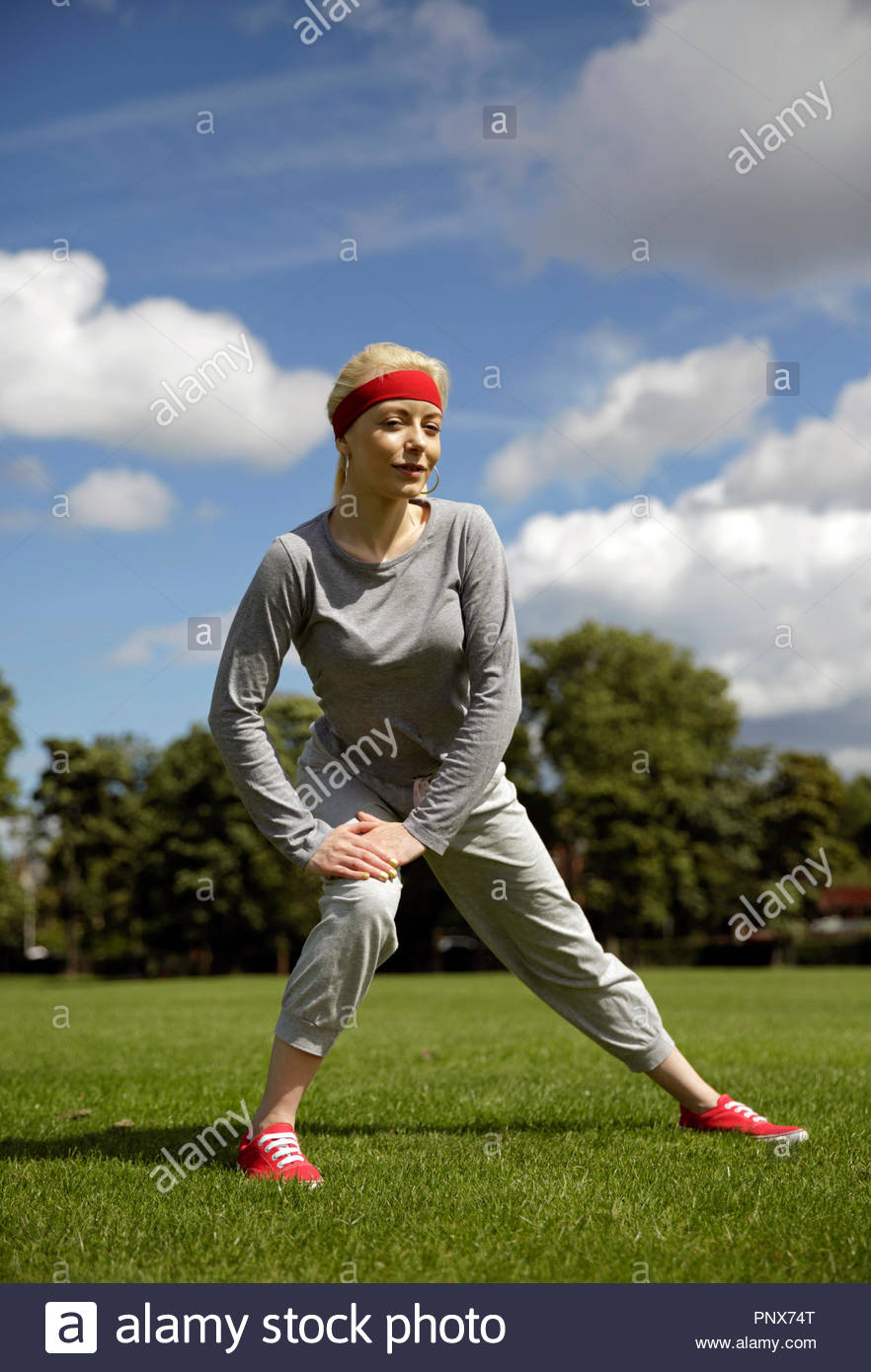 Blonde Frau in einem Trainingsanzug ausführen Stretching Übungen im Park Stockfoto