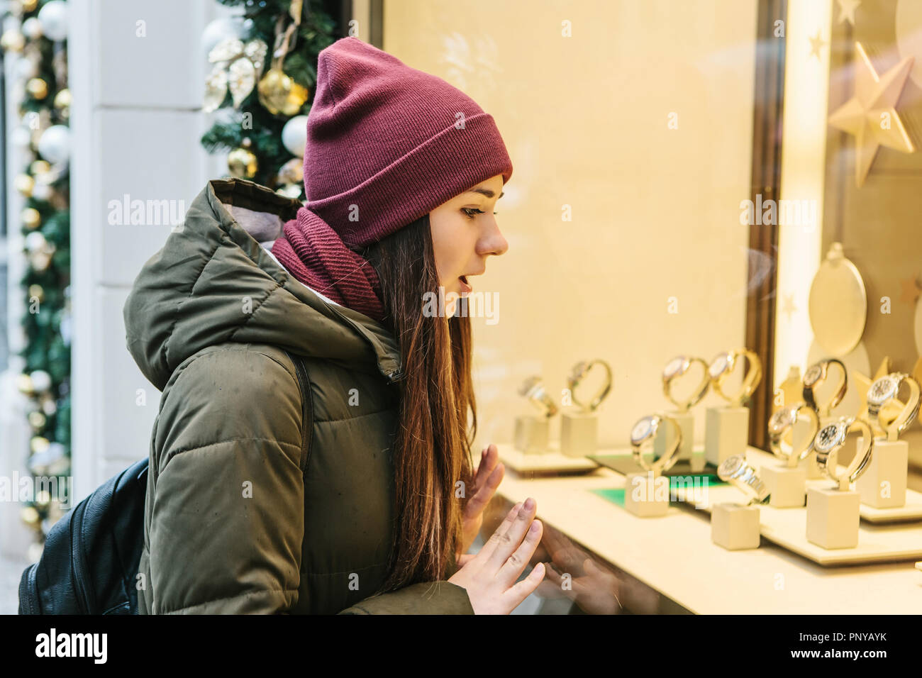 Eine junge schöne Frau oder ein Mädchen schaut durch ein Schaufenster während der Weihnachtsferien und ist überrascht. Stockfoto