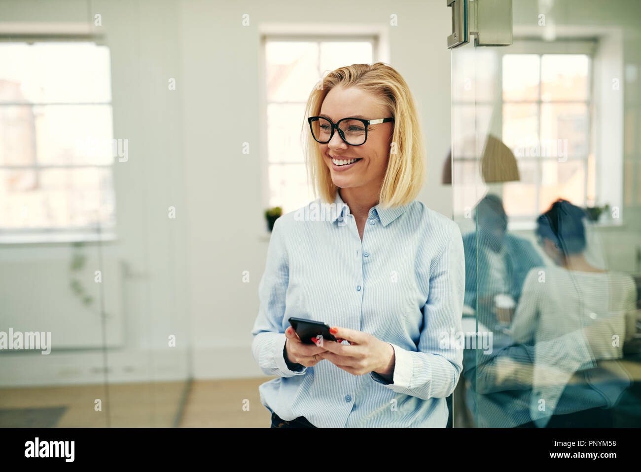 Junge Geschäftsfrau in einem modernen Büro- und Lachen beim Lesen eine lustige SMS-Nachricht auf Ihr Handy Stockfoto