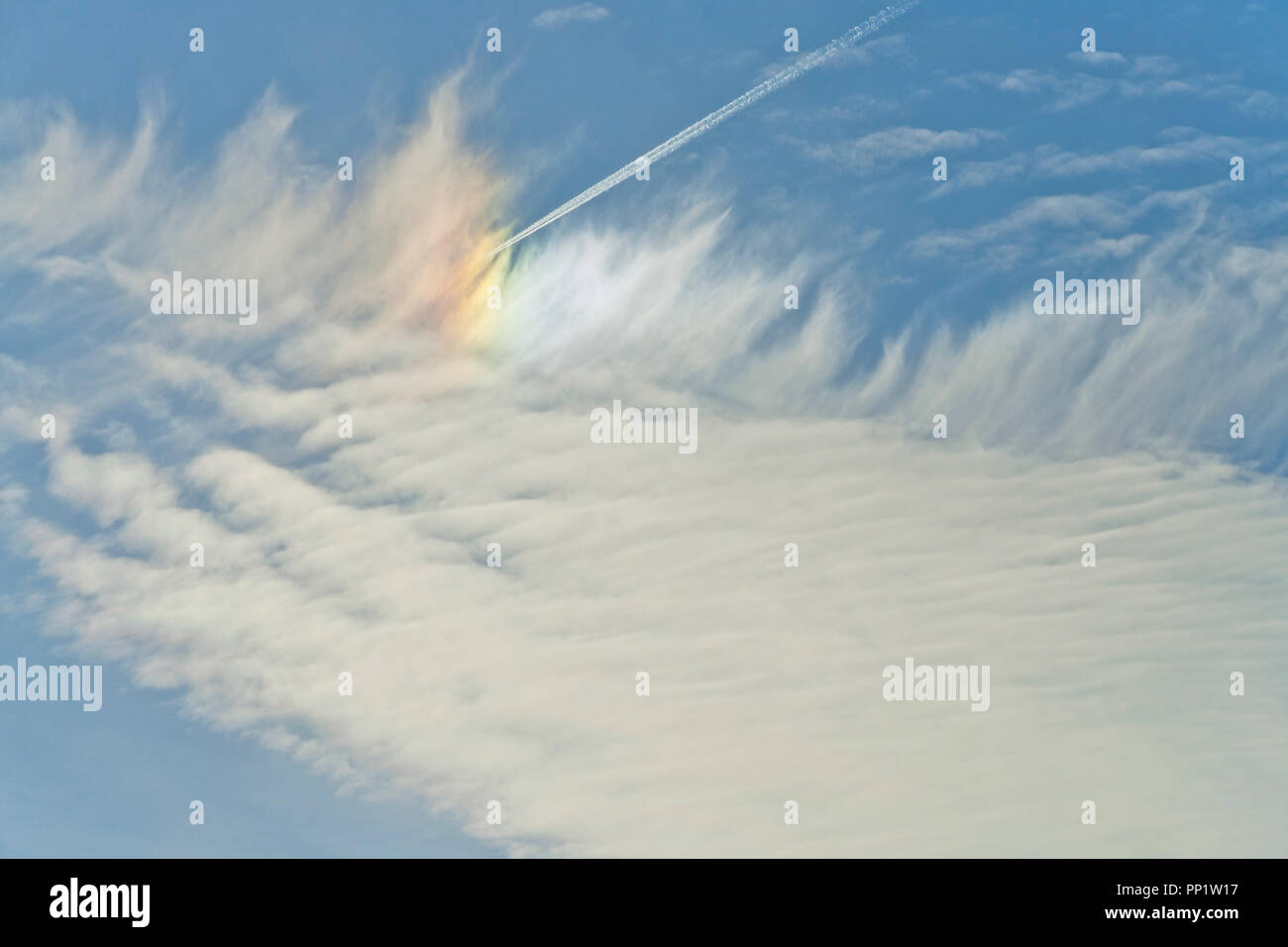 Ein Flugzeug fliegt unter Feder-wie Cirrus Wolken brechende Sonnenlicht eine nebensonne gegen ein indigo Hintergrund Ende Dezember zu erstellen. Stockfoto