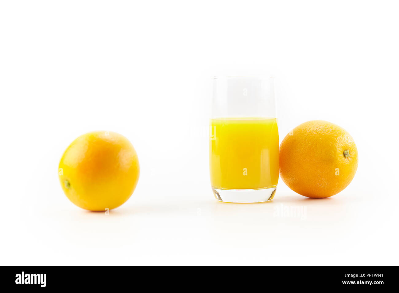 Zwei Orangen und ein Glas Orangensaft auf weißem Hintergrund. Stockfoto