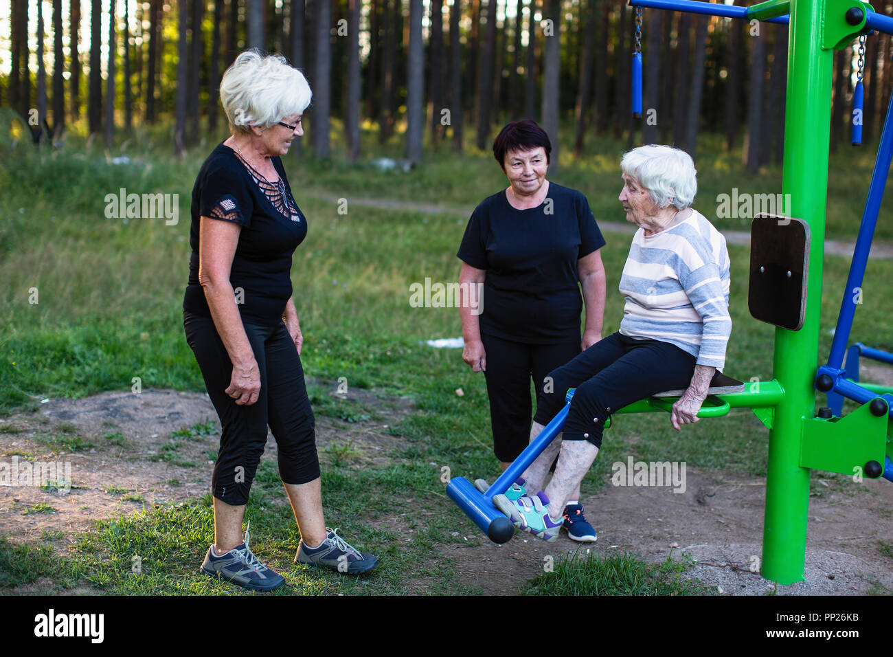 Ältere Frau auf einer Sport Simulator, zwei Frauen helfen, ihre Übungen zu tun. Stockfoto