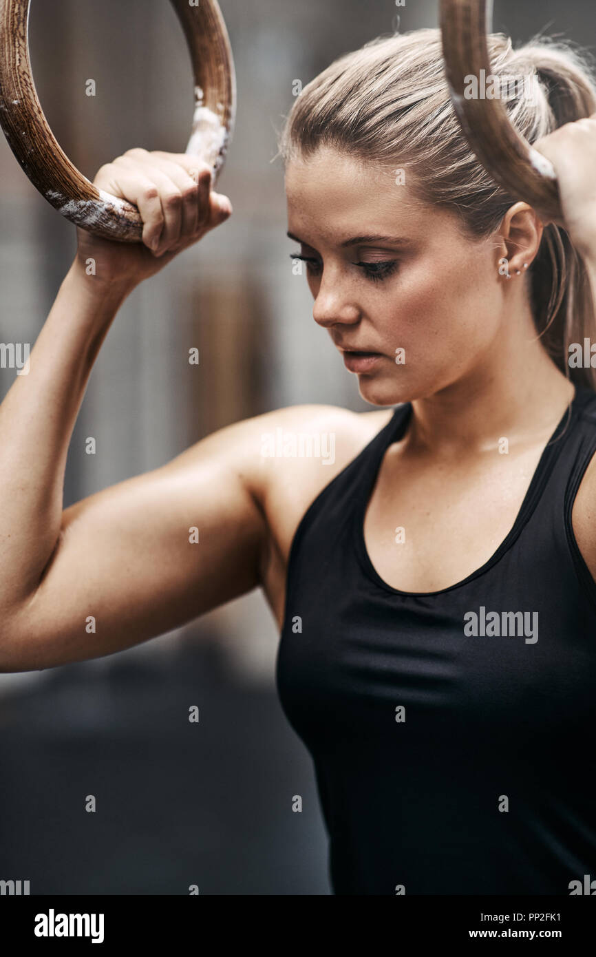 Passen junge Frau in Sportkleidung bei der Ausübung auf Ringe während eines Training Session in einem Fitnessstudio konzentriert Stockfoto