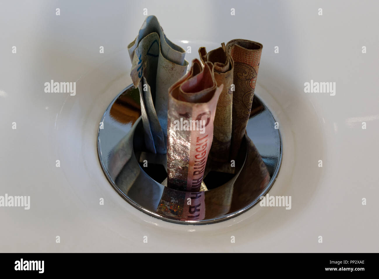 Asiatische und Afrikanische Notizen eine verchromte Stecker Bohrung in einem weißen Keramik Waschbecken - werfen Geld in den Sand gesetzt, verschwenderisch Stockfoto