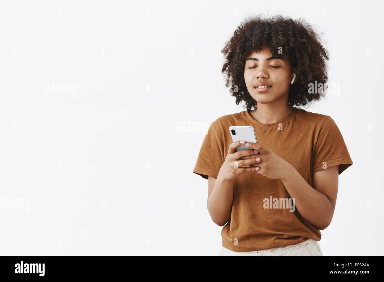 Mädchen führte weg von fantastischen Klang der Musik im Ohr. Ruhig und entspannt sorglos Afrikanische amerikanische Studentin in Braun t-shirt schließen Augen holding Smartphone trägt drahtlose Kopfhörer Stockfoto