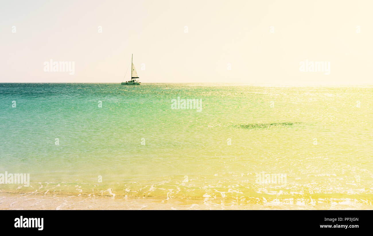 Eine Segelyacht gegen einen ruhigen türkisfarbenen Meer mit Sonnenlicht durchflutet. Ein blauer wolkenloser Himmel an einem hellen Sommertag. Tropische Landschaft Stockfoto