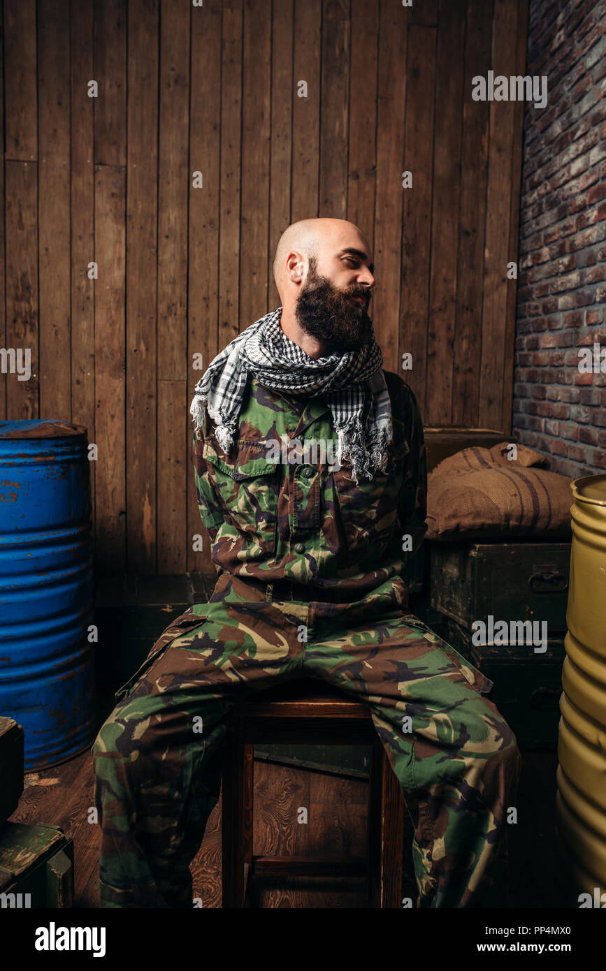 Captive Soldat sitzt auf einem Stuhl, Schrecken des Krieges gebunden. Terrorismus und Terror, militärischen Mann in khaki Camouflage, Barrel Kraftstoff oder Chemikalien auf Backgr Stockfoto