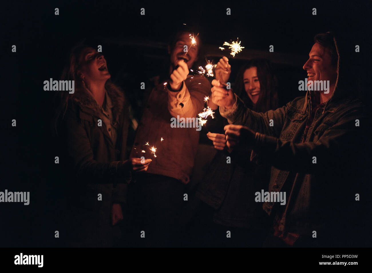 Lächelnde Männer und Frauen spielen mit Feuer glitzert in der Nacht. Freunde feiern Anlass mit Feuerwerk in der Dunkelheit. Stockfoto